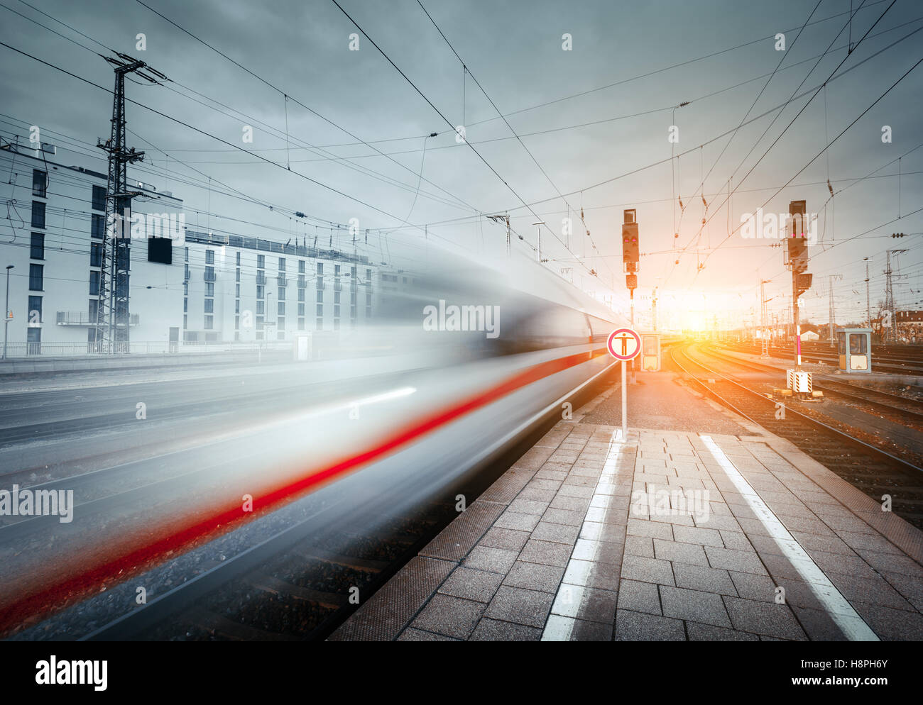 High speed passenger train on railroad track in motion at sunset. Blurred commuter train. Railway platform in the city. Railway Stock Photo