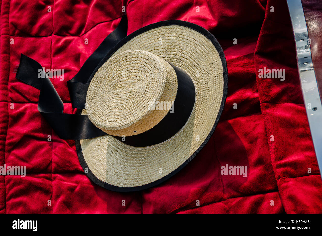 A Gondolier's straw hat resting on a red cover of a Gondola in Venice Stock Photo