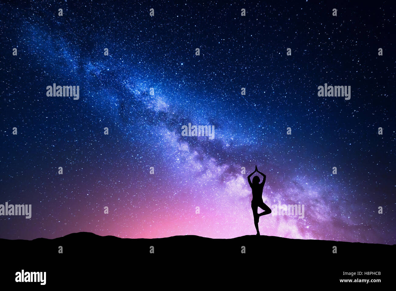 Milky Way with silhouette of a standing woman practicing yoga on the mountain. Beautiful landscape with meditating girl against Stock Photo