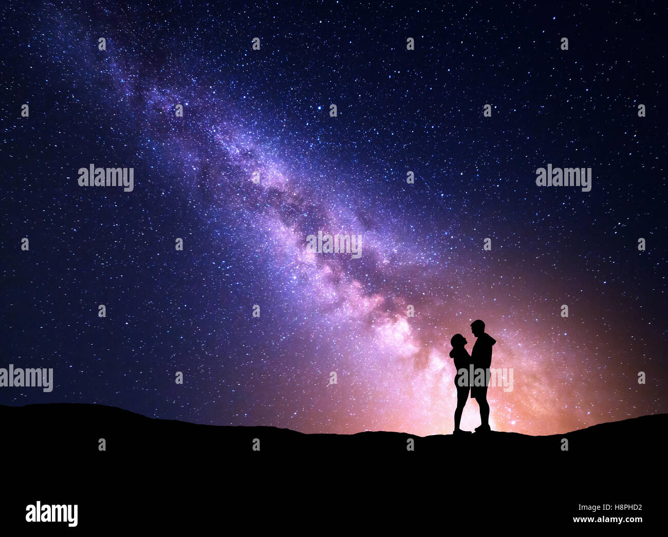 Milky Way with silhouette of people. Landscape with night starry sky. Standing man and woman on the mountain with yellow light. Stock Photo