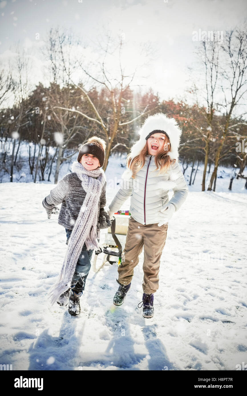 Composite image of brother and sister playing with sled on snow field ...