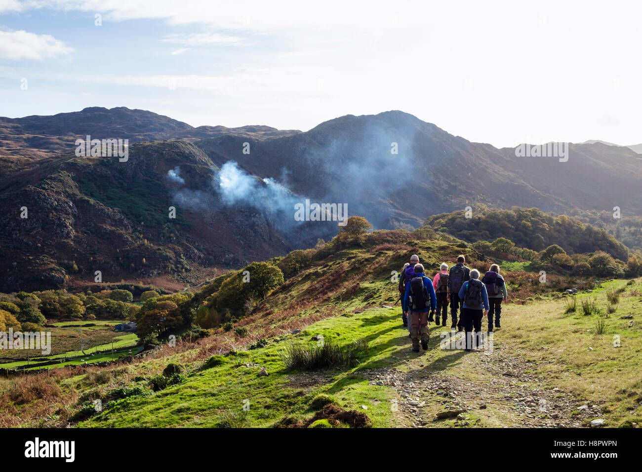 Hikers descending Yr Aran with fires burning to control Rhododendrons across Nant Gwynant valley. Gwynedd Snowdonia National Park Wales UK Stock Photo