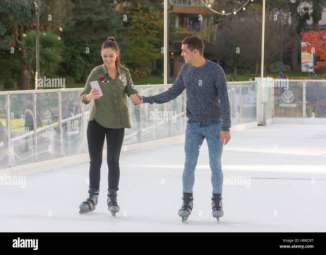 Young couple holding hands while ice skating on an outdoor ice rink, UK