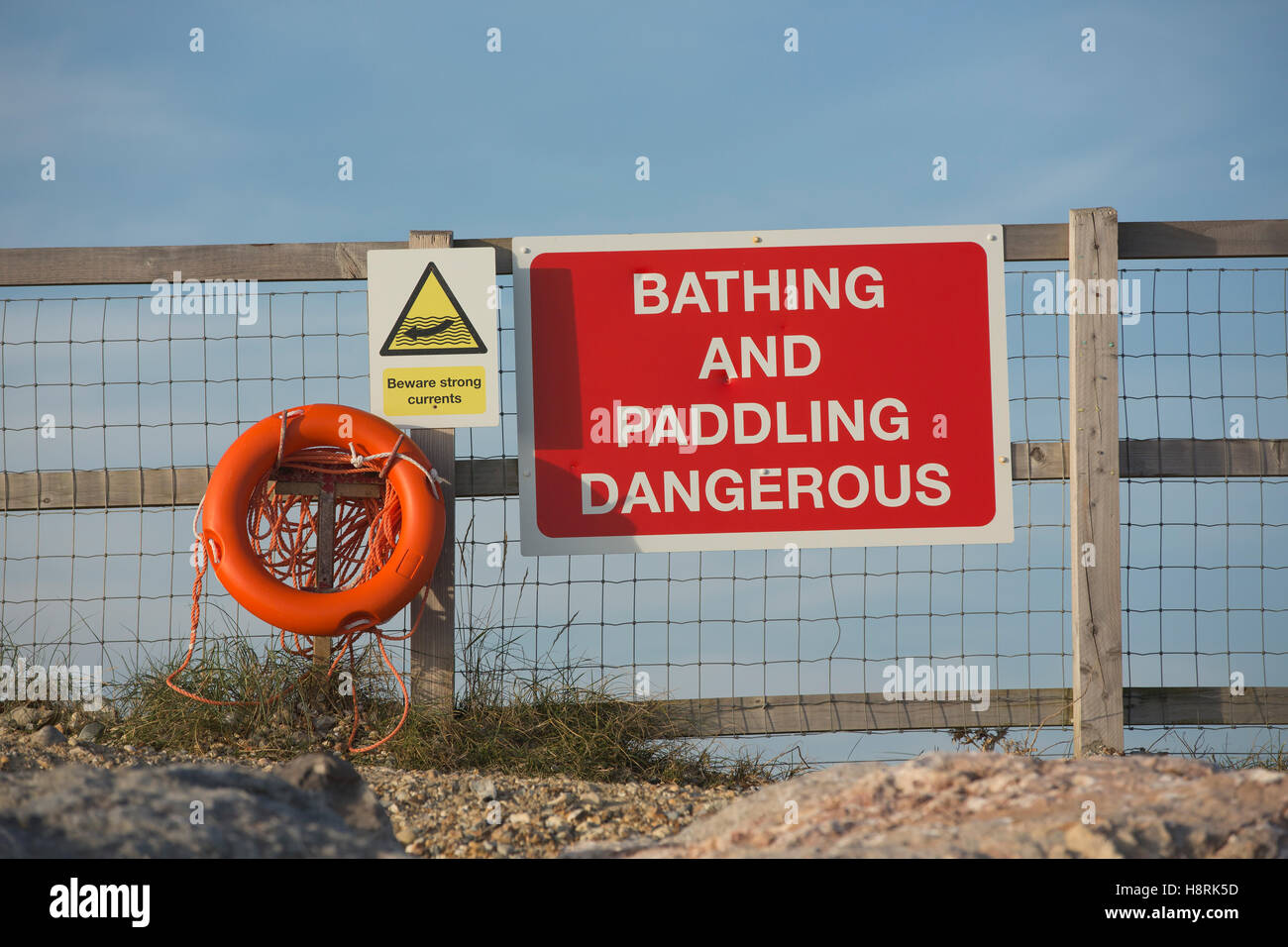 Danger sign on a beach with safety line and life preserver belt. Bathing and Paddling dangerous in white letters on red. Stock Photo