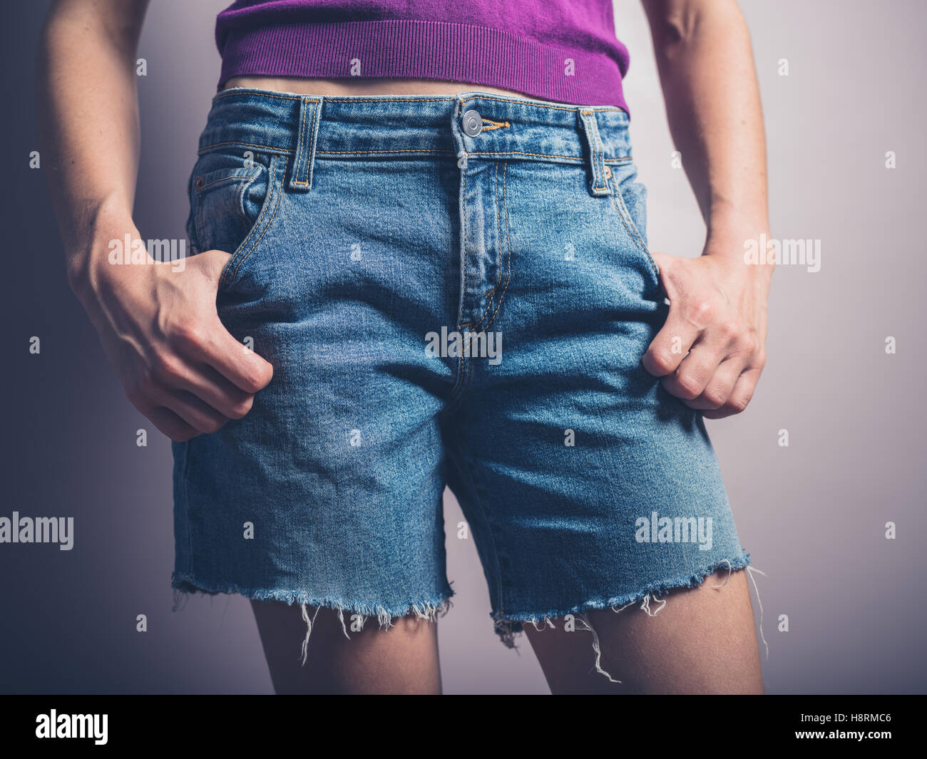 A young woman wearing denim shorts is posing with her hands in her pockets Stock Photo