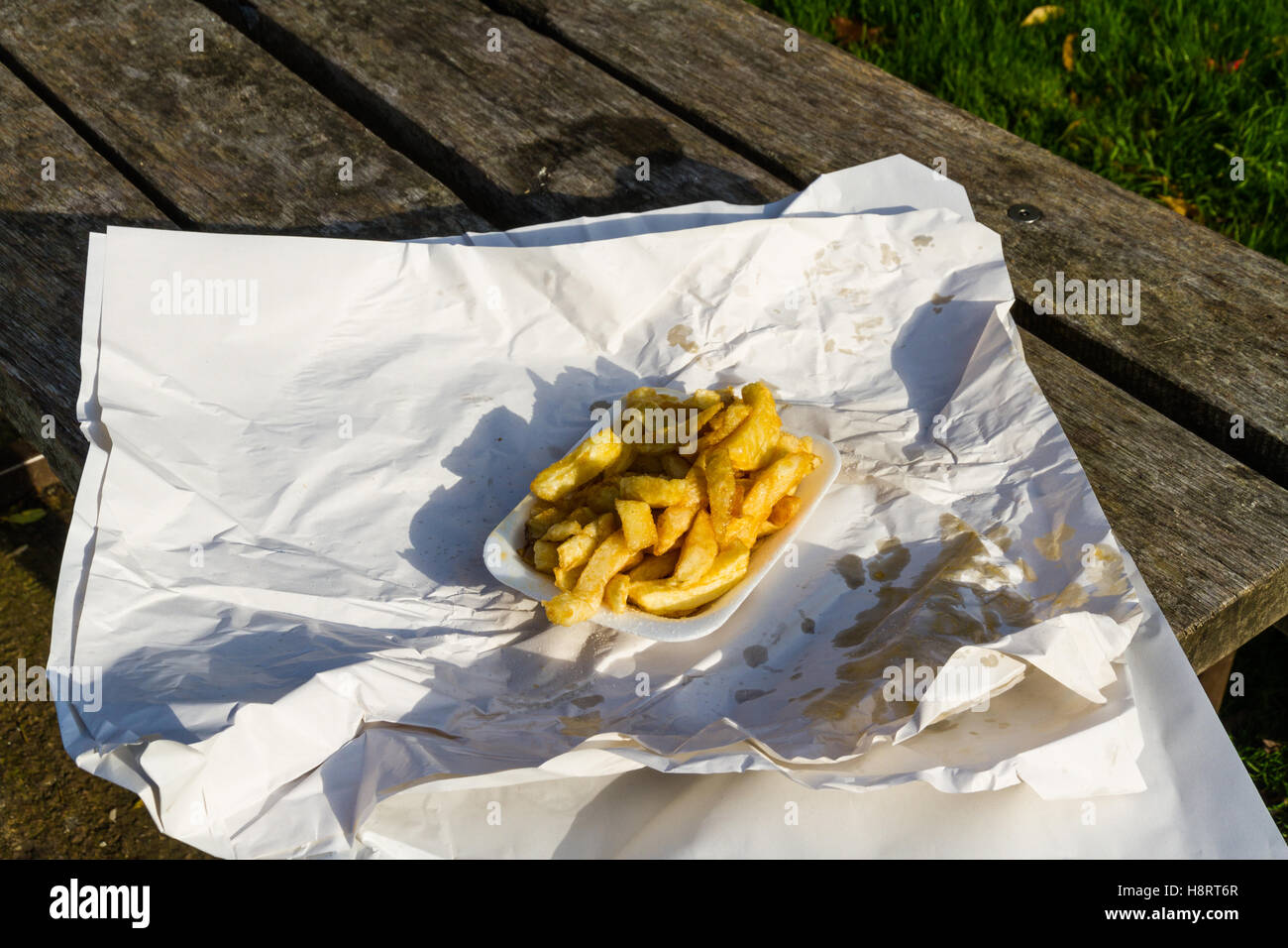 Portion of British chips or fries, in carton with wrapping paper on a sunny day. Stock Photo