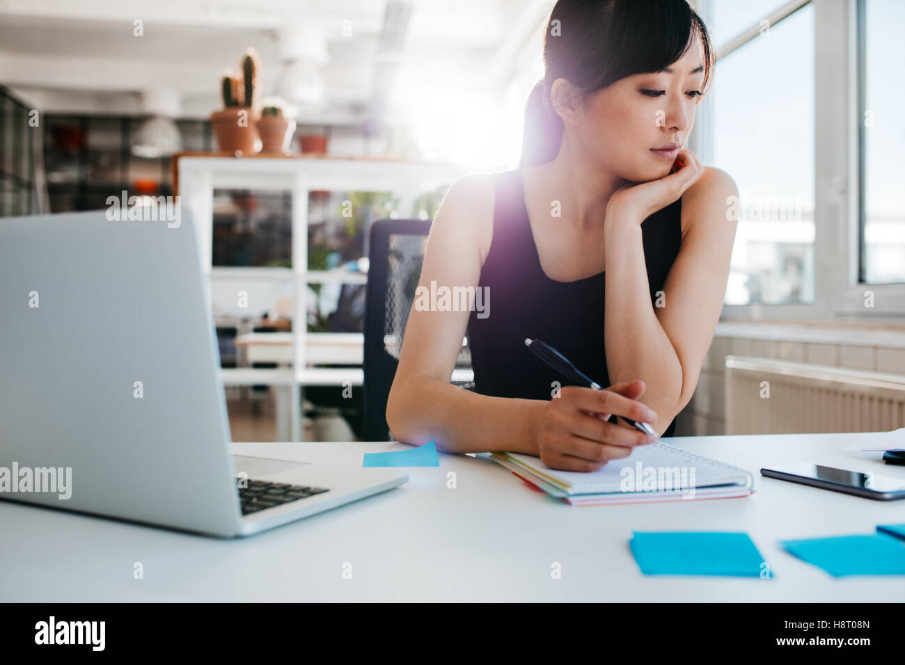 Shot of young asian woman working at her desk, writing notes. Businesswoman at her workplace. Stock Photo