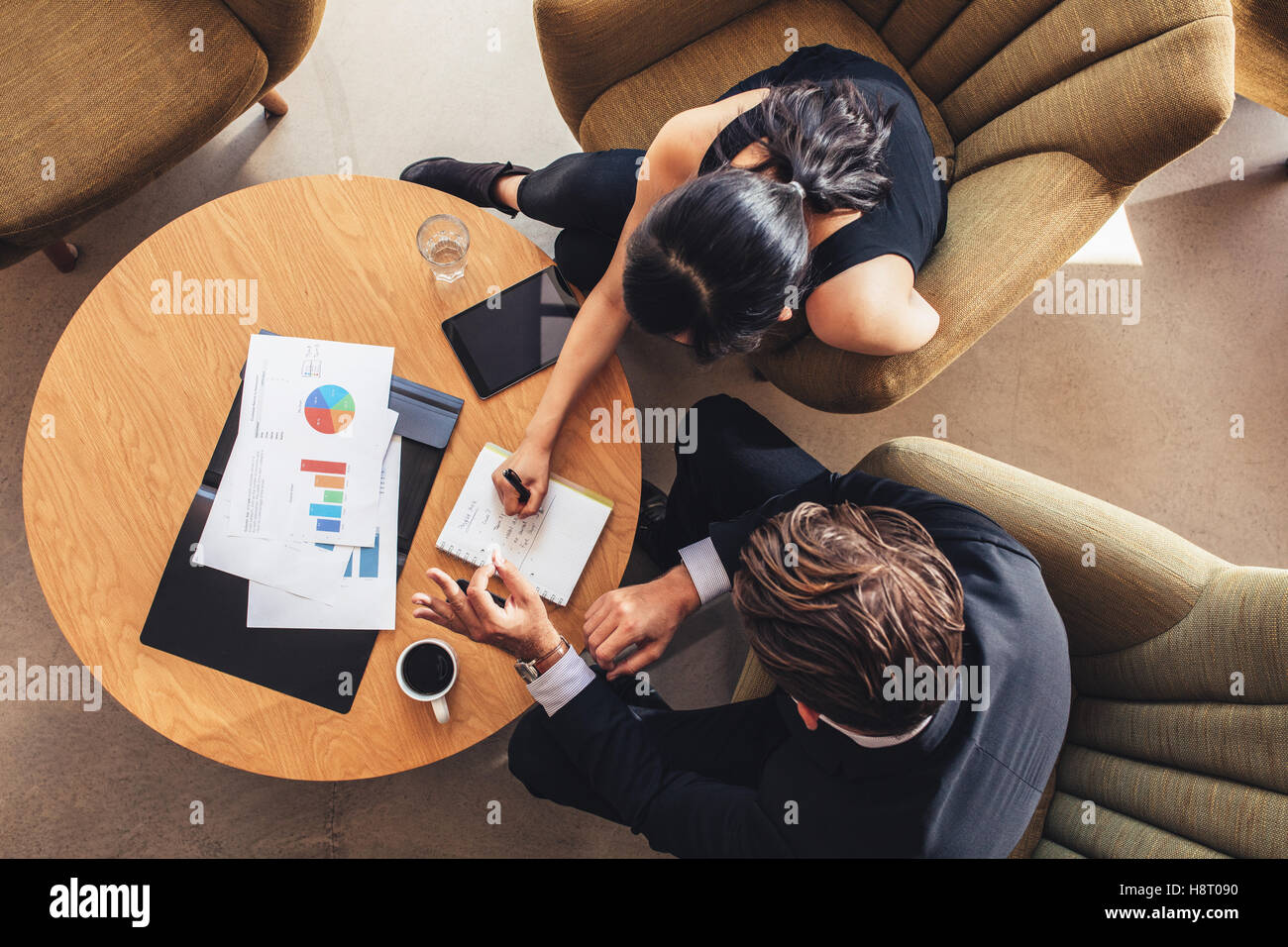 View from above of two business people planning work around table. Businessman and woman going through the to do list while sitt Stock Photo