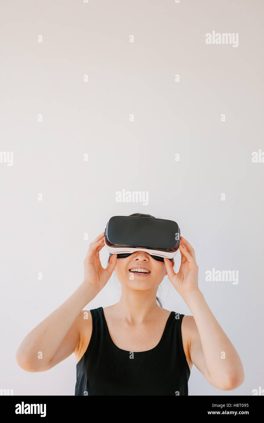 Vertical shot of woman using the virtual reality headset and smiling against grey background. Happy female model wearing VR gogg Stock Photo