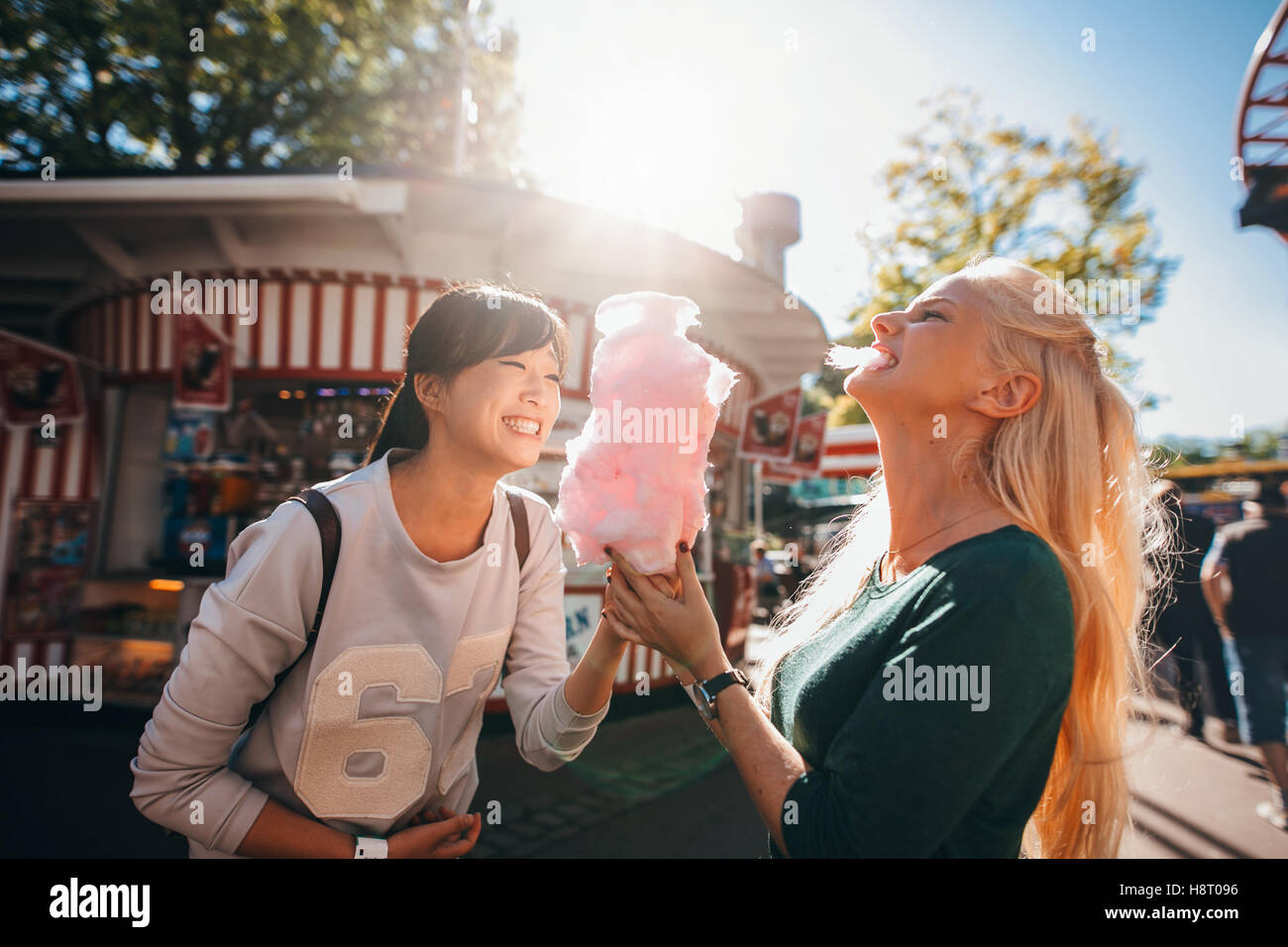 Shot of happy female friends in amusement park eating cotton candy. Two young women enjoying a day at amusement park. Stock Photo