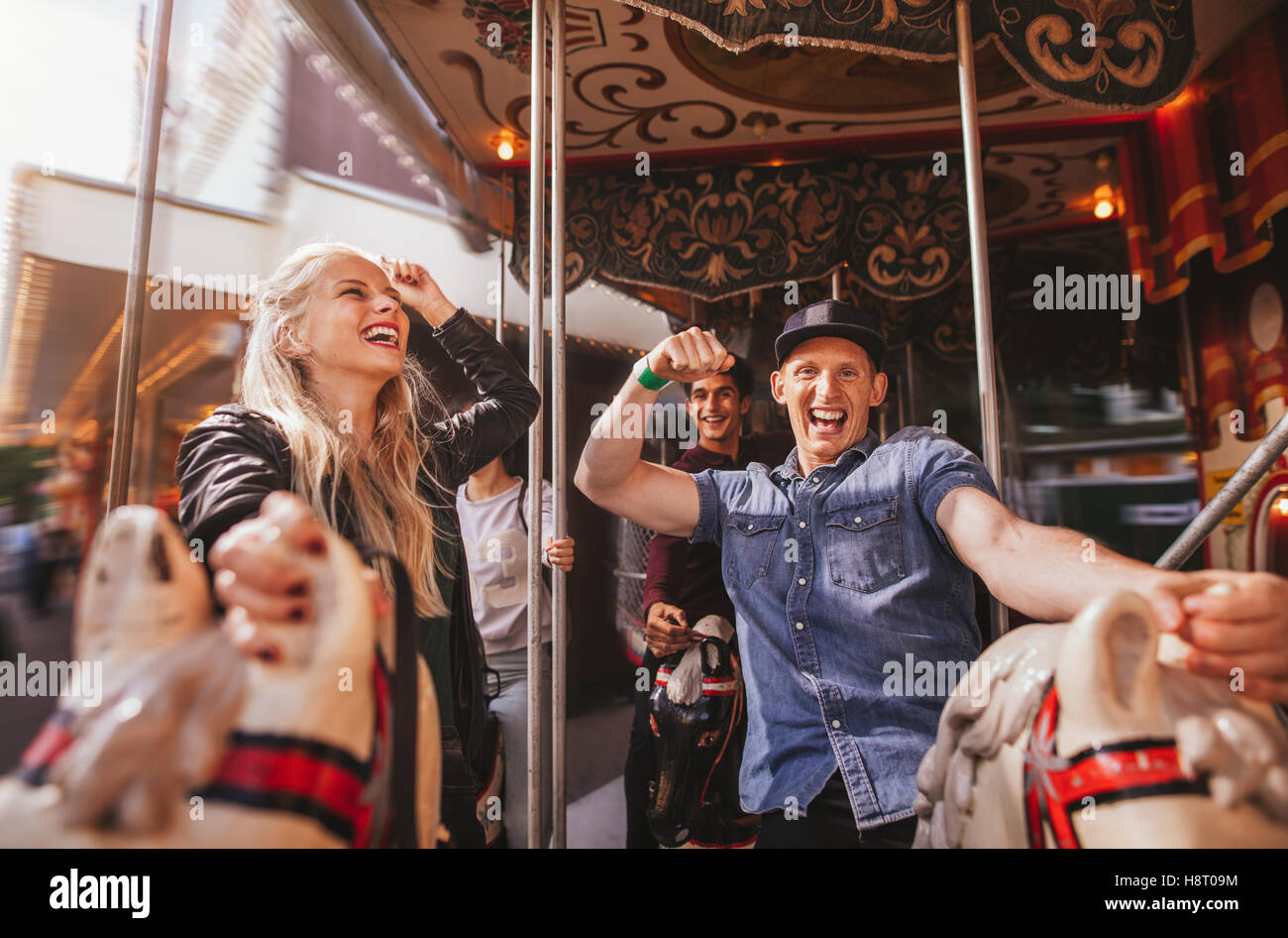 Shot of young people on amusement park ride having fun. Smiling man and woman on horse carousel ride at fairground. Stock Photo