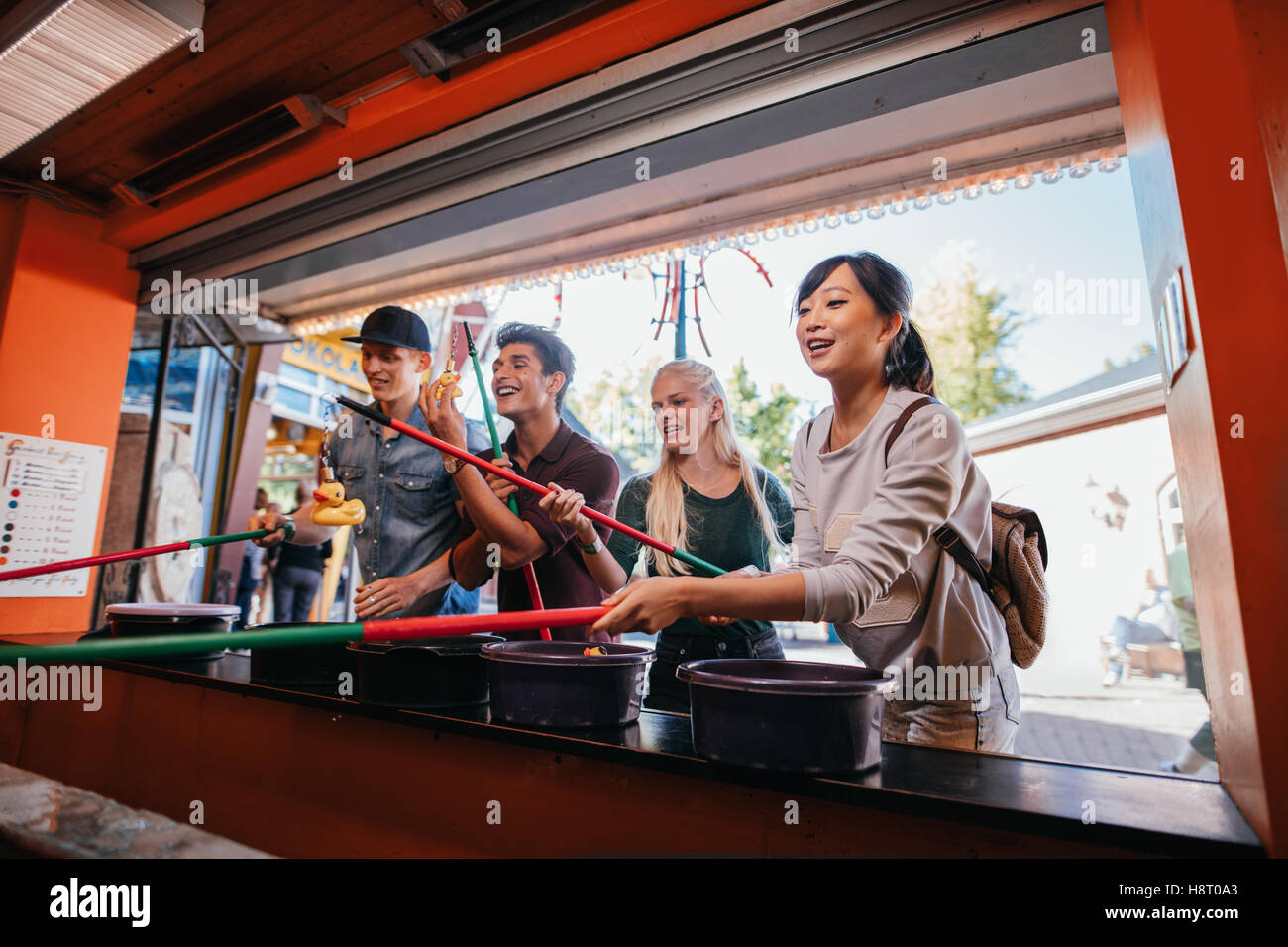 Group of young people having fun with fishing game in amusement park. Multiracial friends playing arcade game. Stock Photo