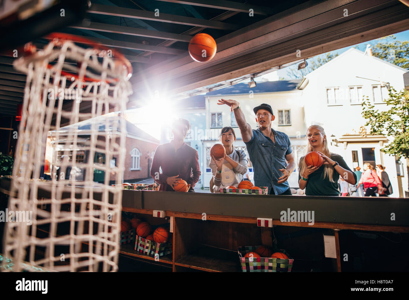 Group of friends shooting hoops at the fair. Young people playing basketball game at amusement park. Stock Photo