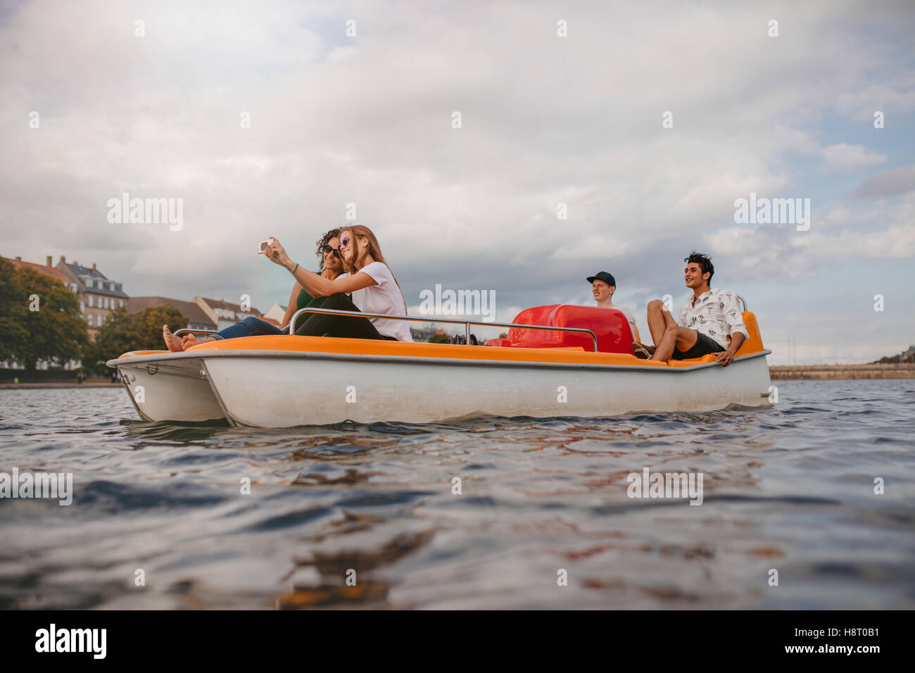 Shot of young friends sitting in pedal boat enjoying holidays. Group of people boating in the lake taking selfie. Stock Photo