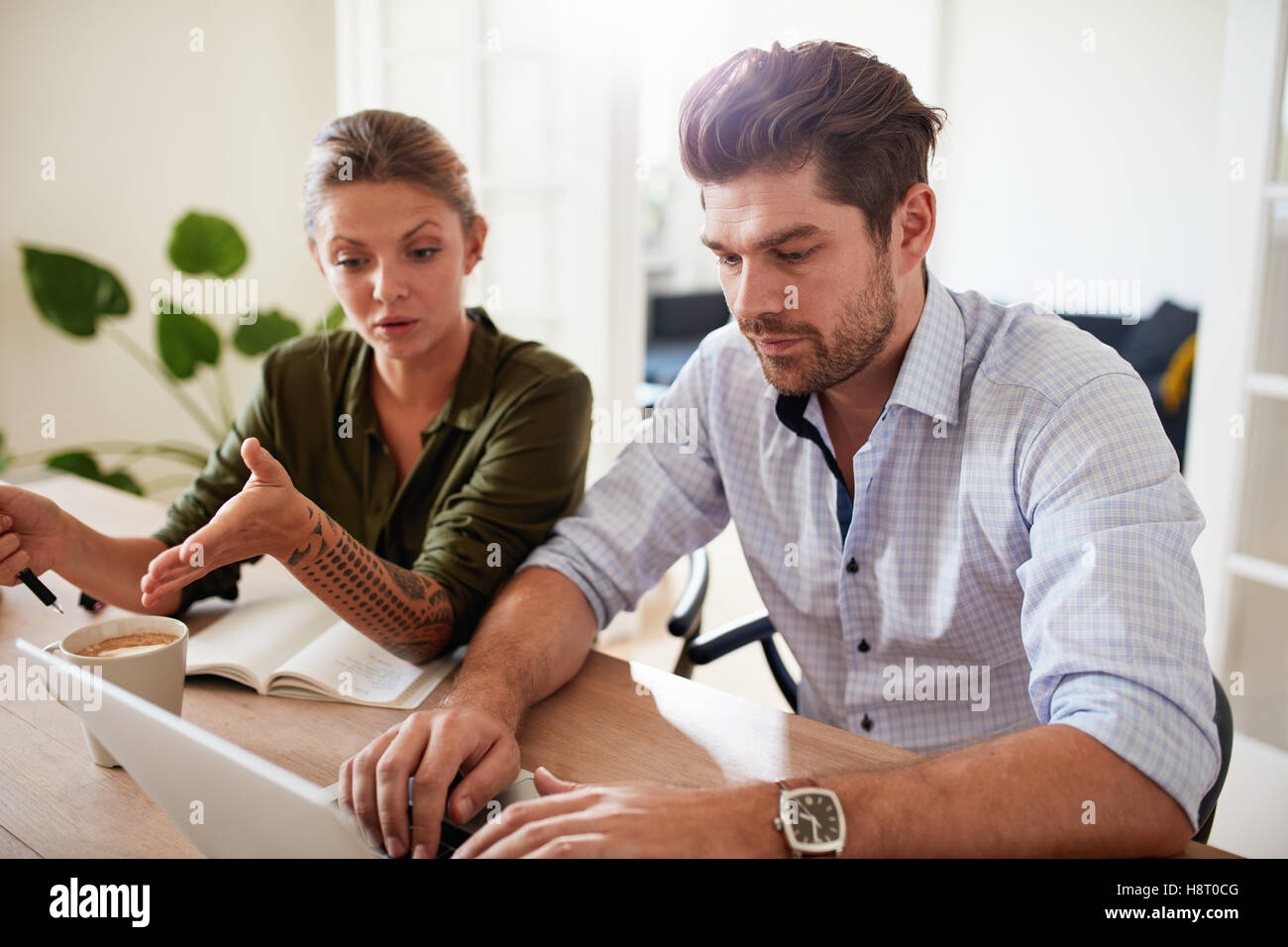 Indoor shot of man and woman sitting at table and working on laptop. Two people using laptop at home office. Stock Photo