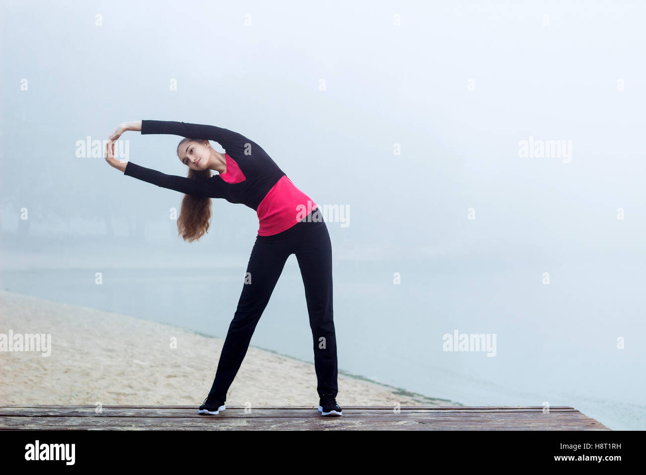 Young pretty slim fitness sporty woman does stretching exercises during training workout outdoor Stock Photo