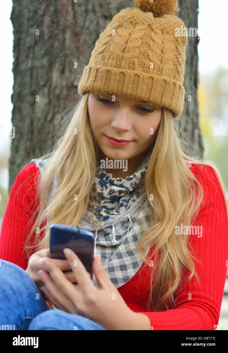 Trendy young woman in fall in park texting Stock Photo