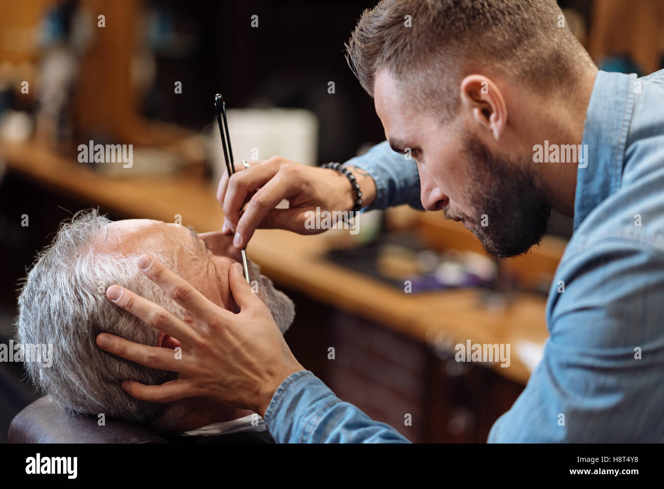Attractive hairdresser is shaving male beard with the knife Stock Photo