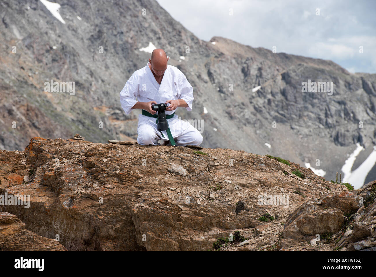The man in a kimono sits in  lotus position on top of  mountain and watching the pictures in the camera. Stock Photo