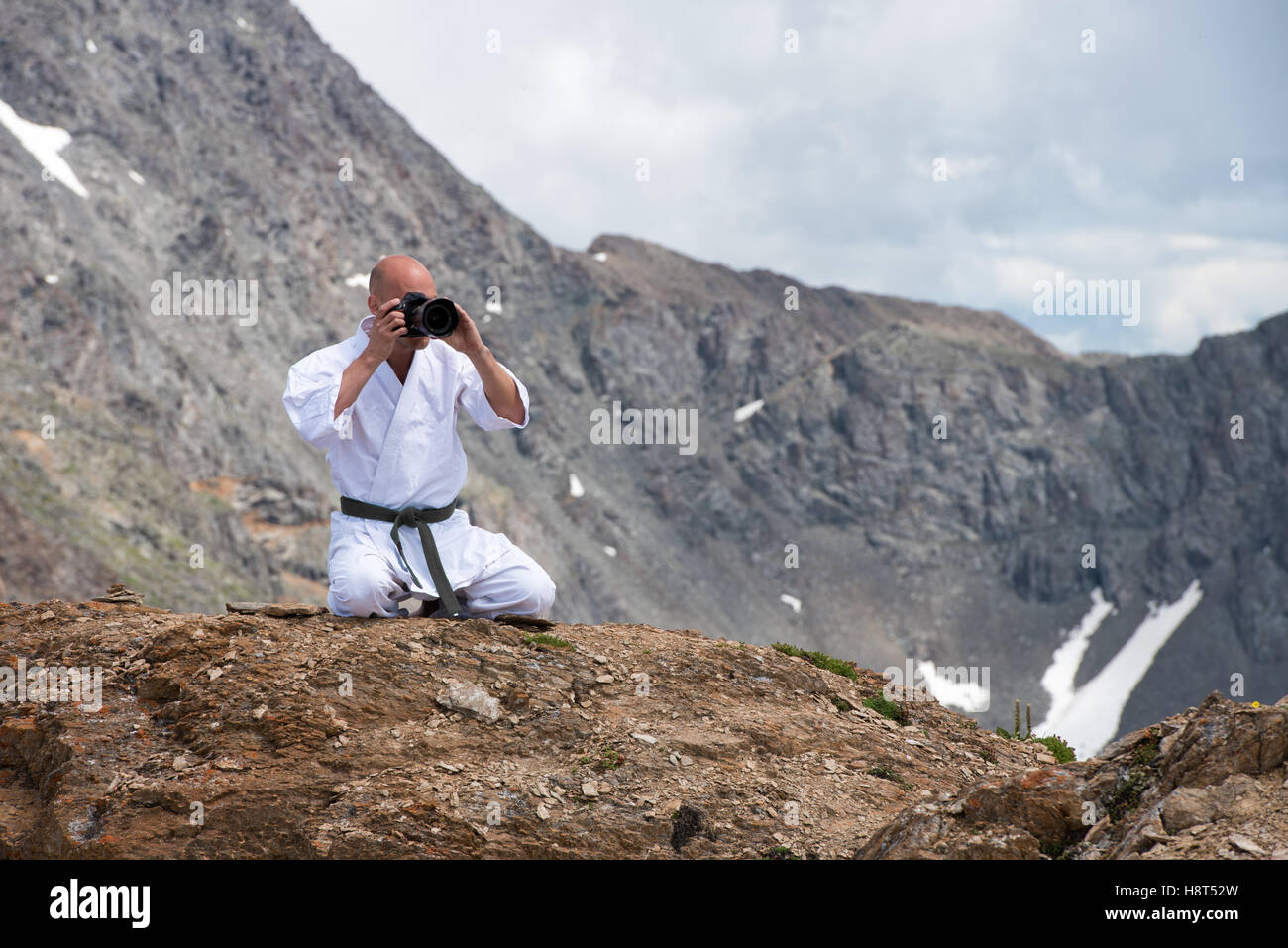 The man in a kimono sits in  lotus position on top of  mountain and taking pictures  the camera. Stock Photo