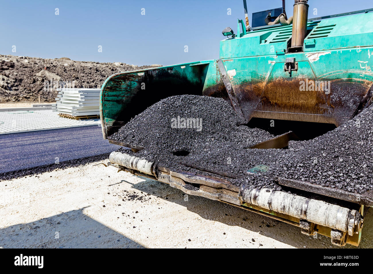Front view on asphalt laying machine full of fresh asphalt at road construction site. Hot asphalt is spreading from paver machin Stock Photo