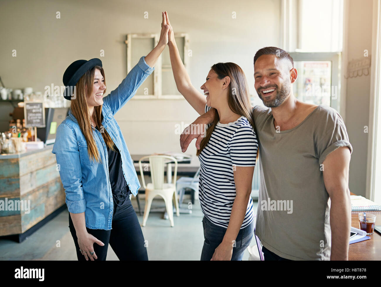 Two women putting up high fives with bearded handsome male friend standing next to them in coffee house Stock Photo