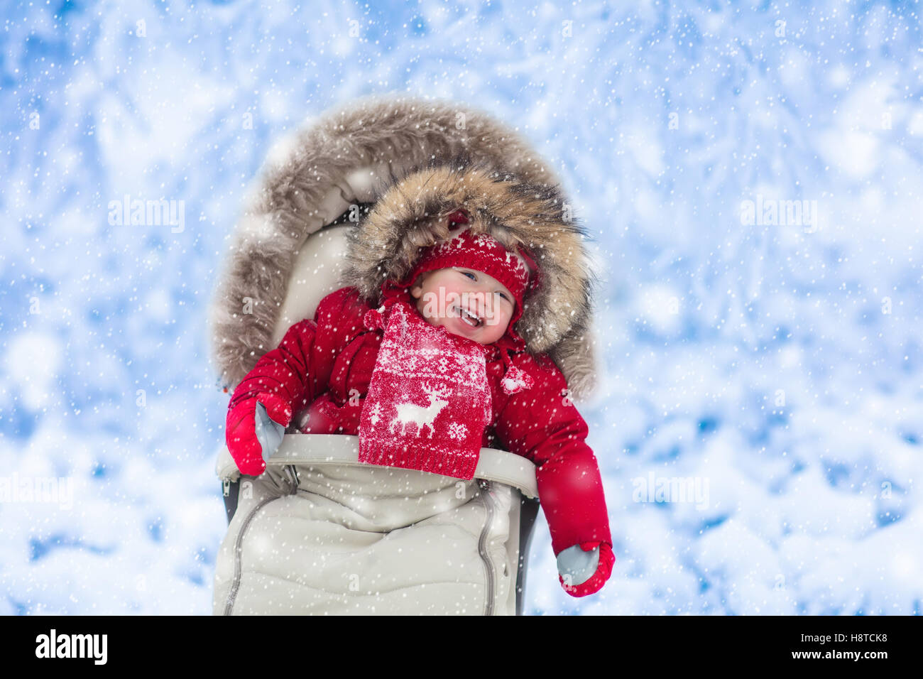 Happy laughing baby in warm red down jacket and knitted Nordic hat and