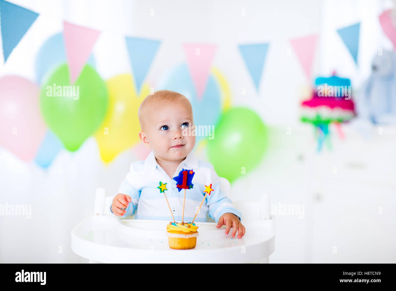 Adorable baby boy celebrating first birthday blowing candles on colorful cup cake. Kids birthday