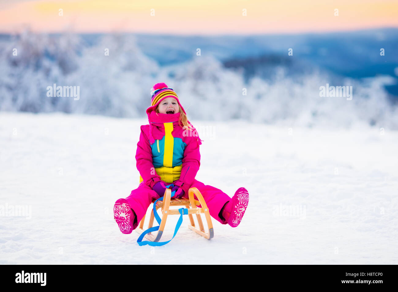 Little girl enjoying sleigh ride. Child sledding. Toddler kid riding a