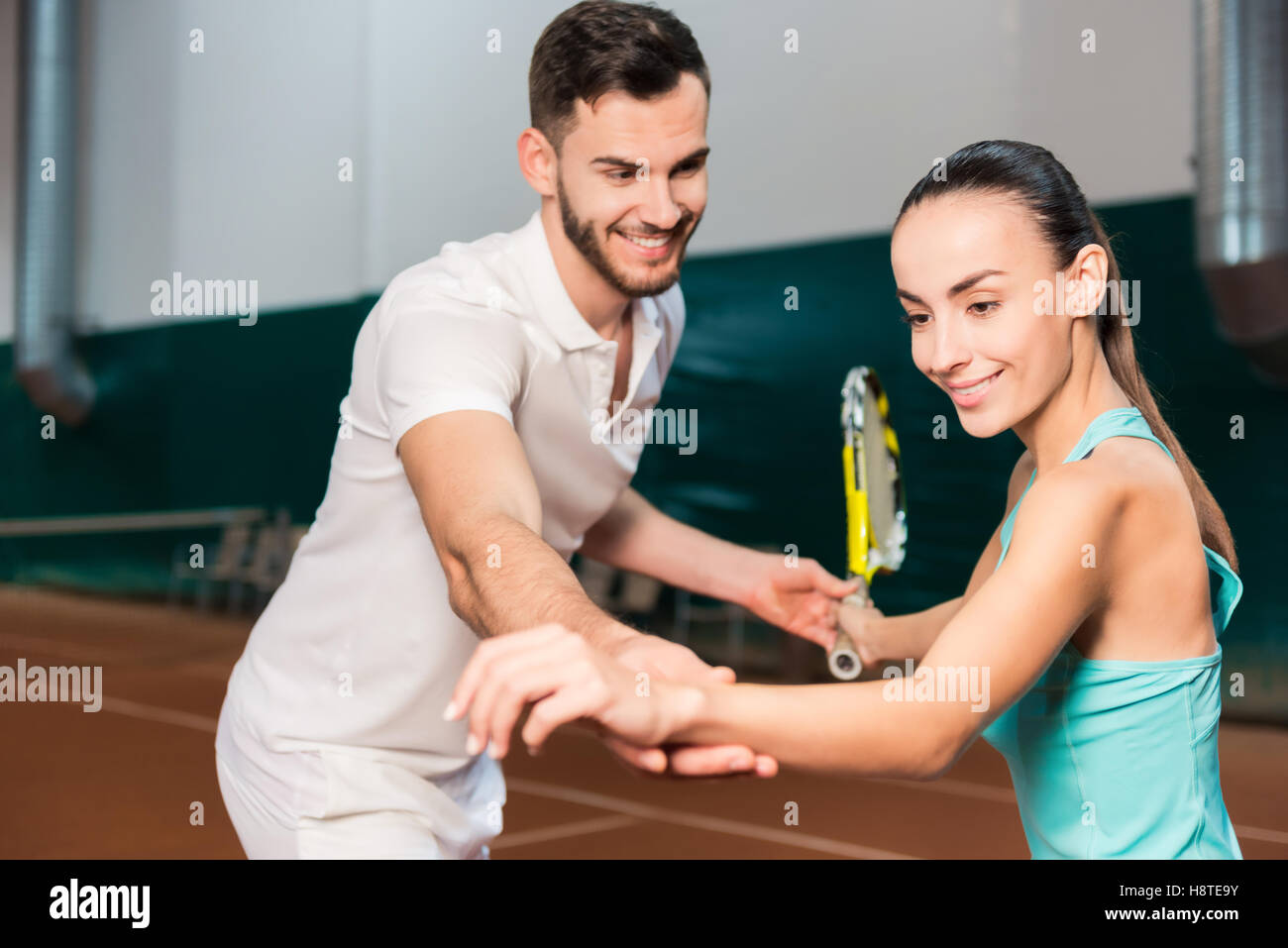 Professional positive instructor teaching a young woman to play tennis