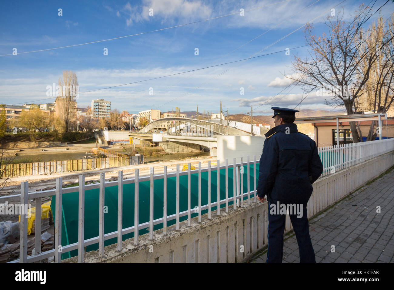 Kosovo Policeman observing Ibar bridge in Mitrovica, symbol of the division between the Albanian and Serbian parts of the city Stock Photo