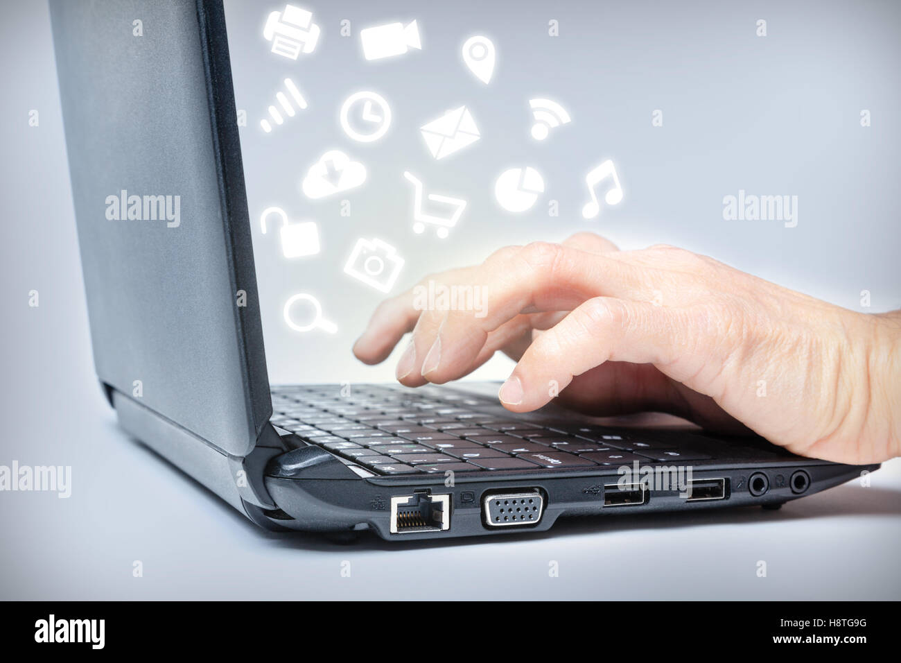 Hands typing on keyboard with common media icons rising from laptop. Multi-tasking on the Internet. Stock Photo