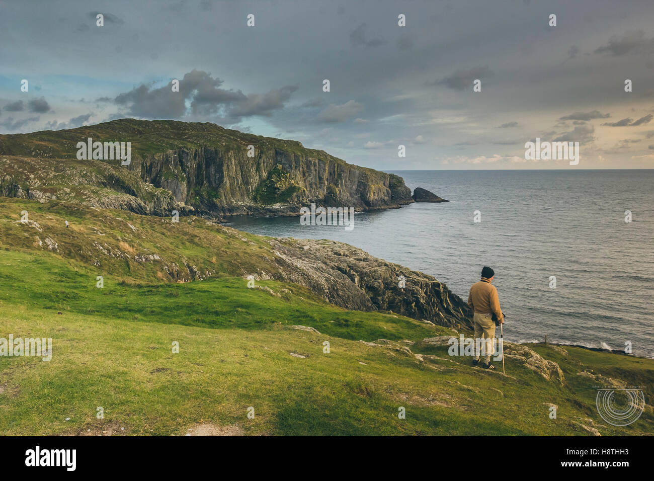A man standing at the edge of a cliff overlooking the ocean with the ...