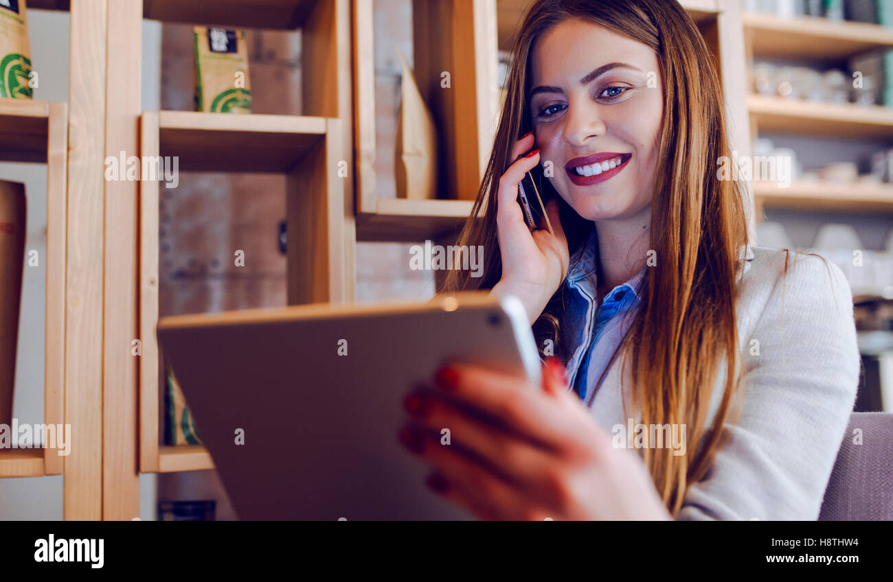 Beautiful Young Woman Talking on Phone and Looking at Tablet Stock Photo