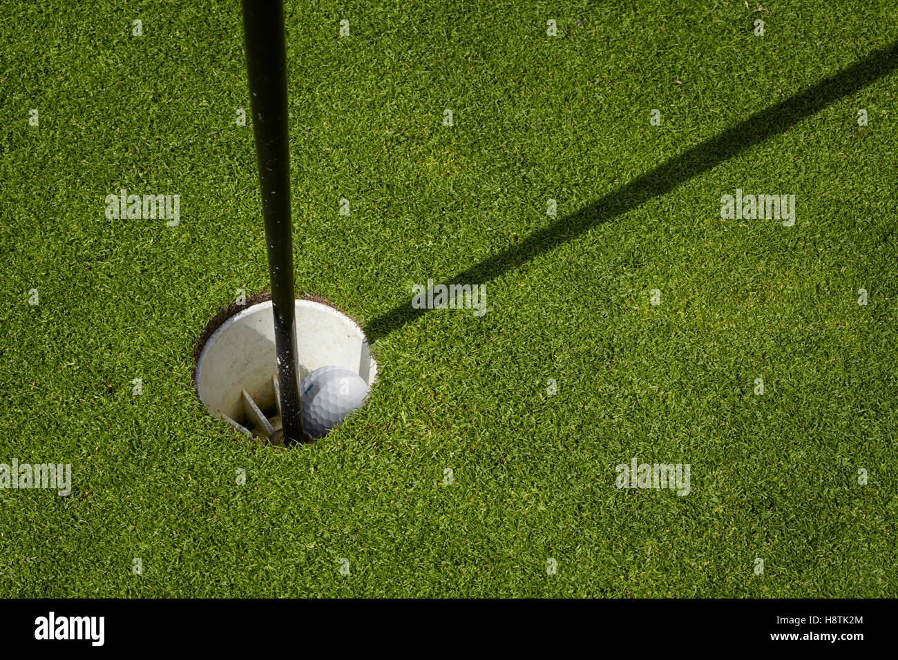 Golf ball inside a cup on a golf course. Putting a green with flag. Stock Photo