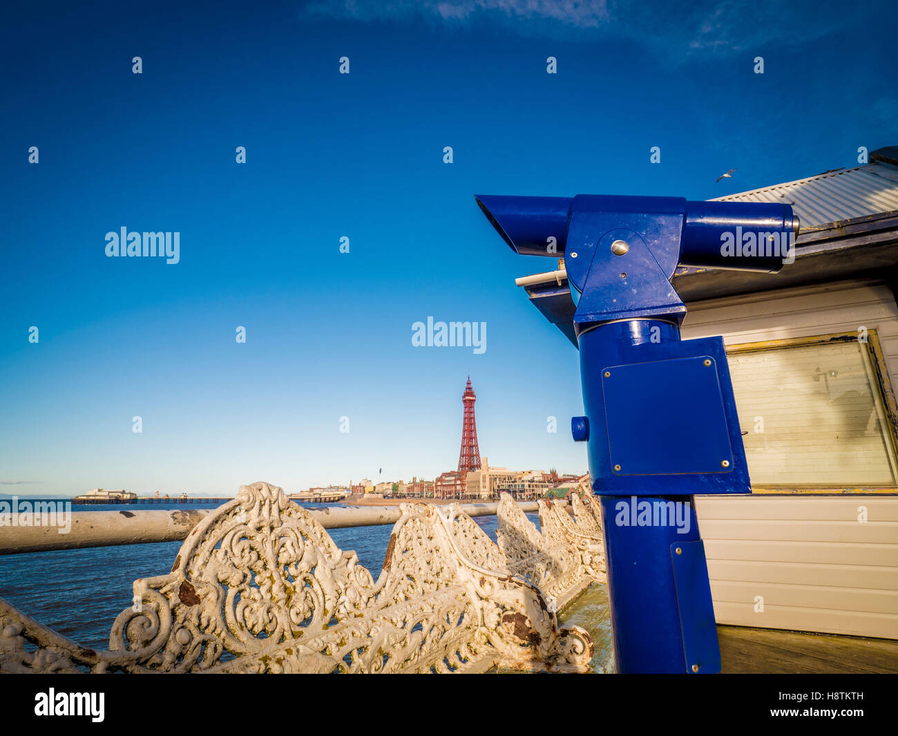 Traditional cast iron seats and Pay to View telescope on Pier, with Blackpool Tower in distance, Blackpool, Lancashire, UK. Stock Photo