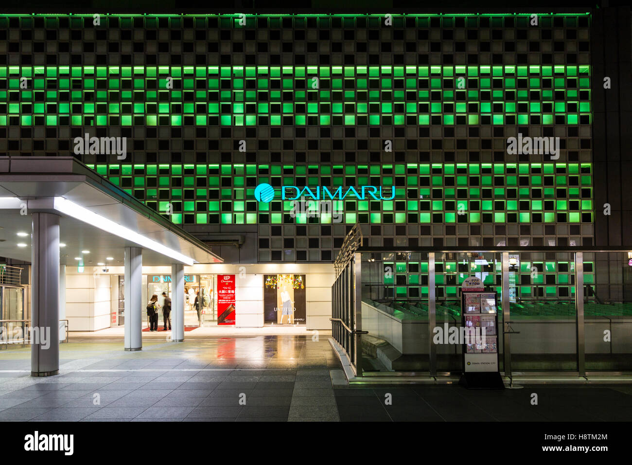 Japan, Osaka Station City. South Gate Building with entrance to Daimaru Department store and illuminated wall with store logo and name. Night time. Stock Photo