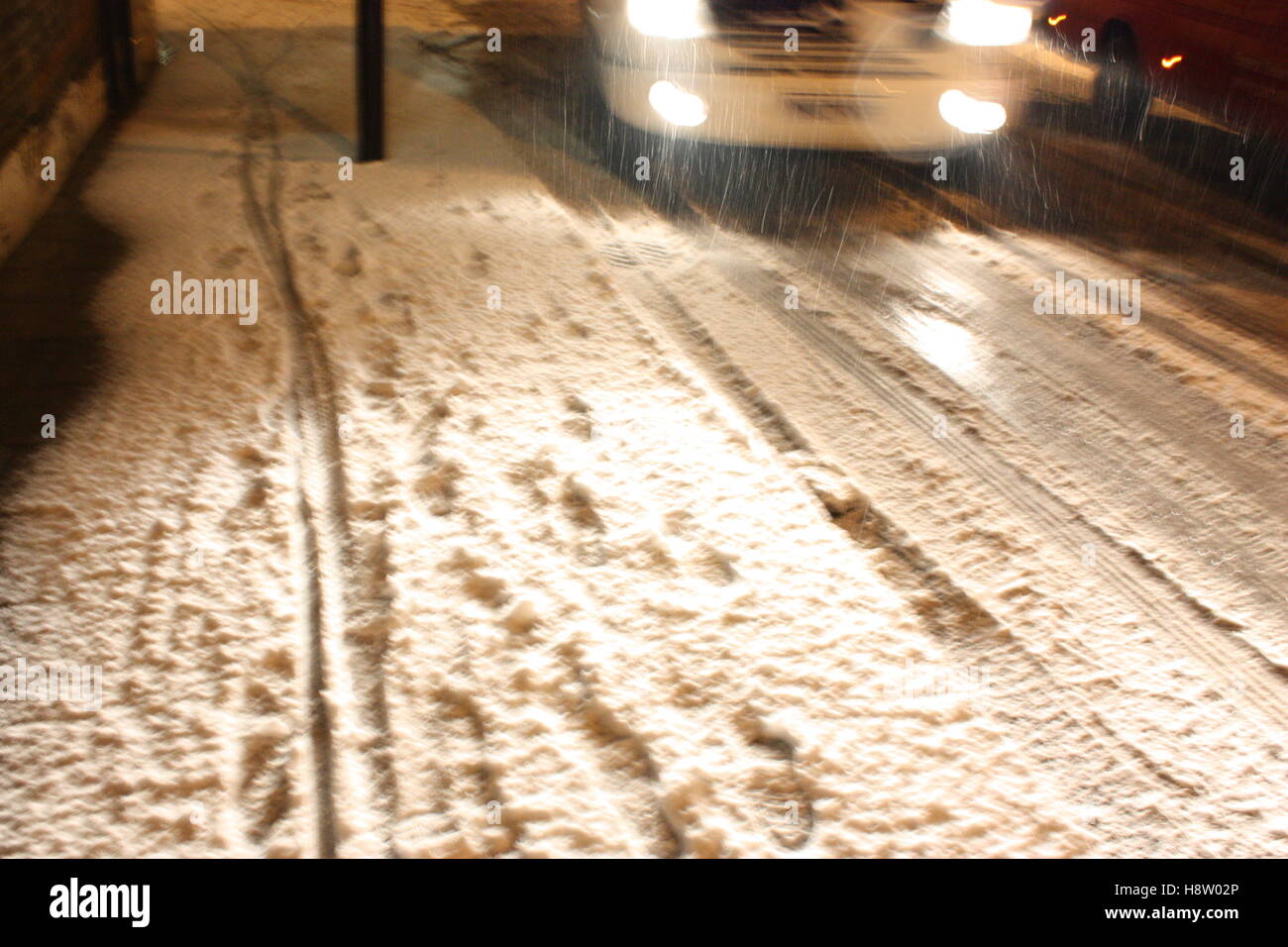 footprints and bike tyre tracks in the snow with headlights lighting up the road Stock Photo
