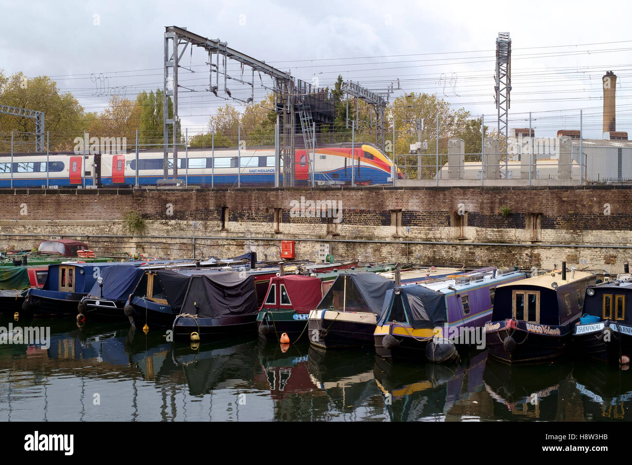 The Regents Canal at St Pancras in London.  A locomotive from East Midlands Trains besides a canal basin of moored narrowboats. Stock Photo
