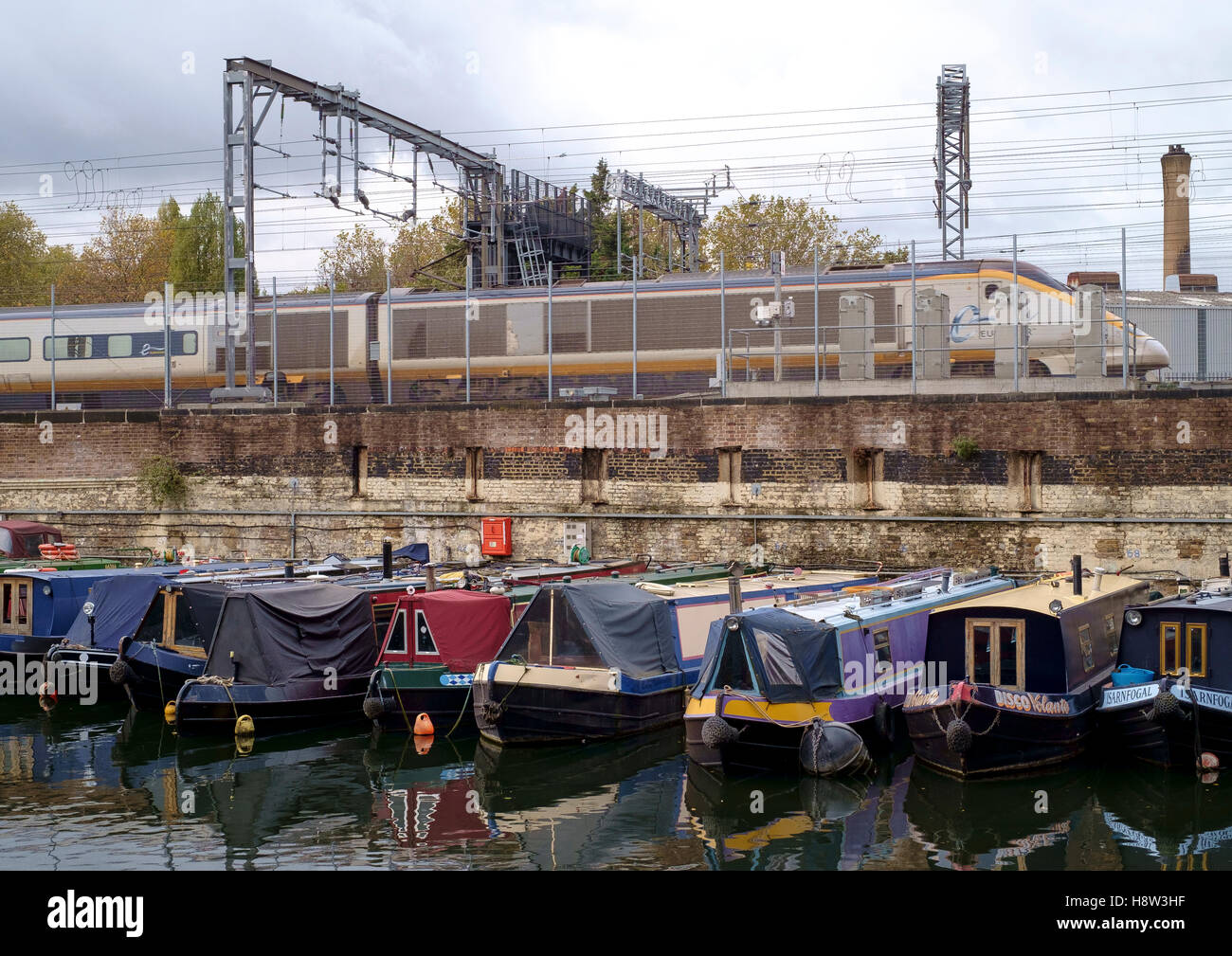 The Regents Canal at St Pancras in London.  A Eurostar train runs  besides a canal basin of moored narrowboats. Stock Photo