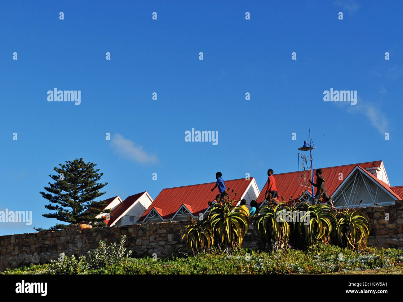 South Africa: children walking in single file on a stone wall in Port Elizabeth, The Friendly City or The Windy City, with red roofs on the background Stock Photo