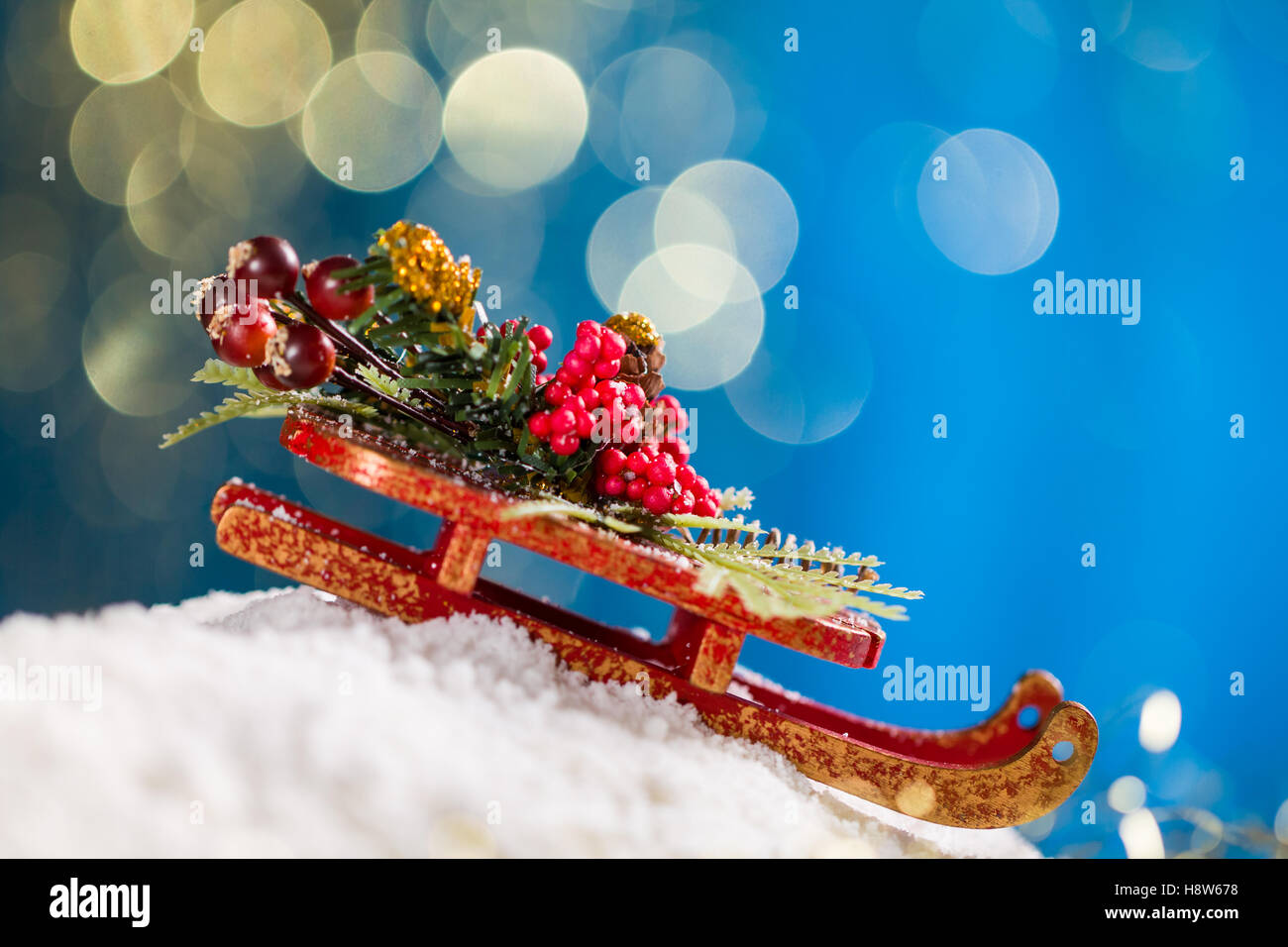 Sleigh with Christmas decoration on snow at blue background with gold glitter. Stock Photo