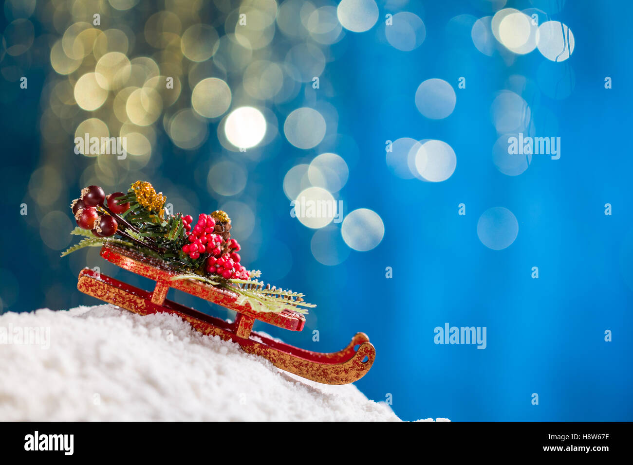 Sleigh with Christmas decoration on snow at blue background with gold glitter. Stock Photo