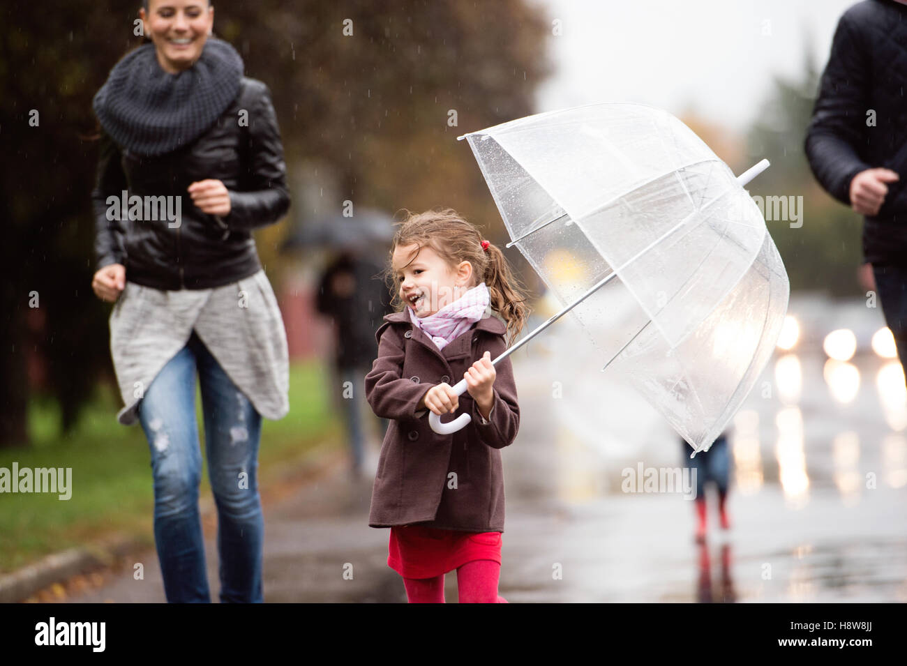 Little girl under the umbrella with her family, running. Rainy d Stock Photo