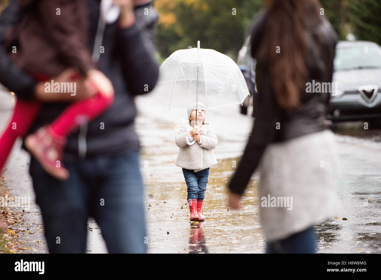 Little girl under the umbrella with her family, walking. Rainy d Stock Photo