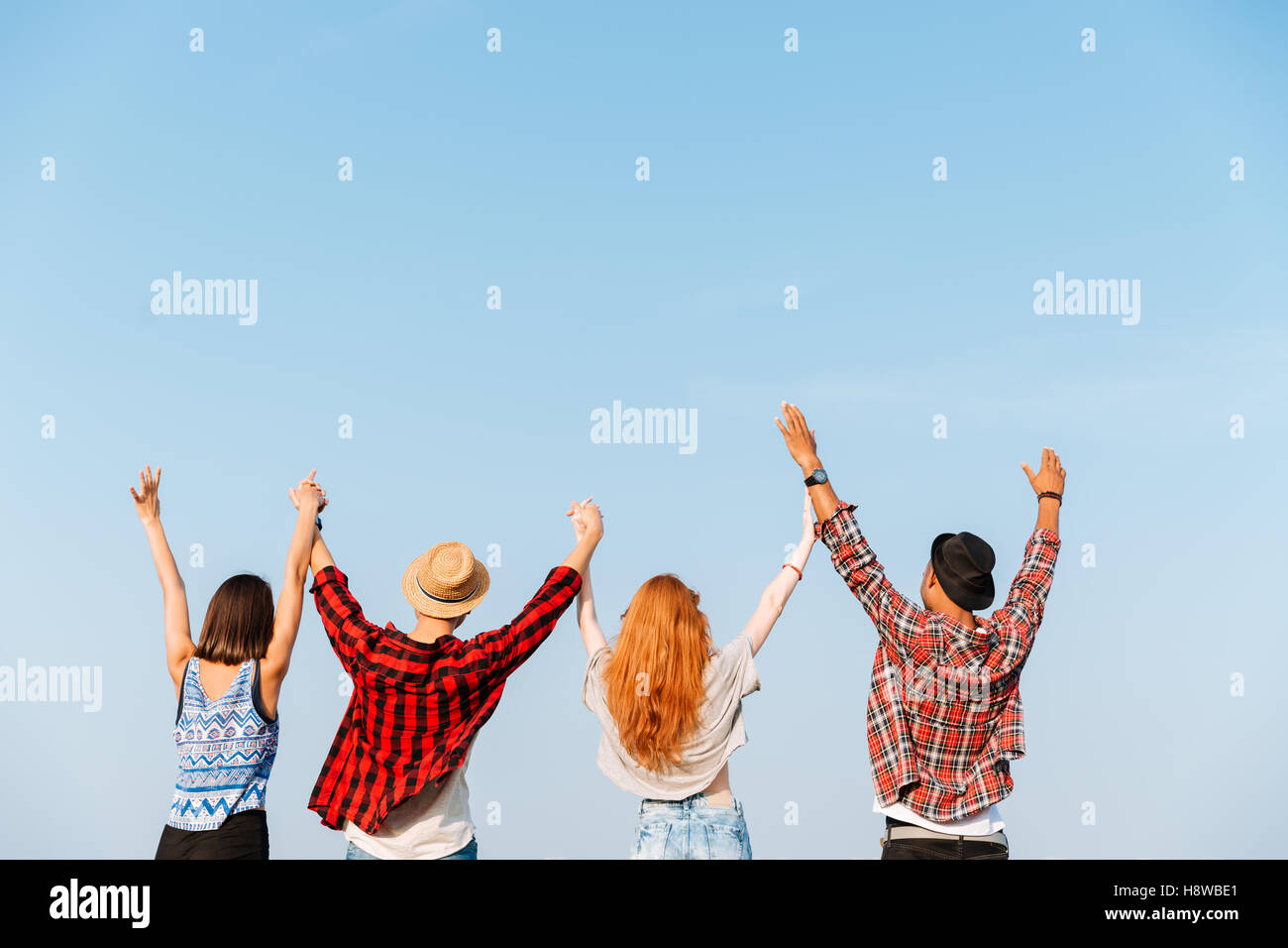 Back view of group of four young people standing and holding raised ...