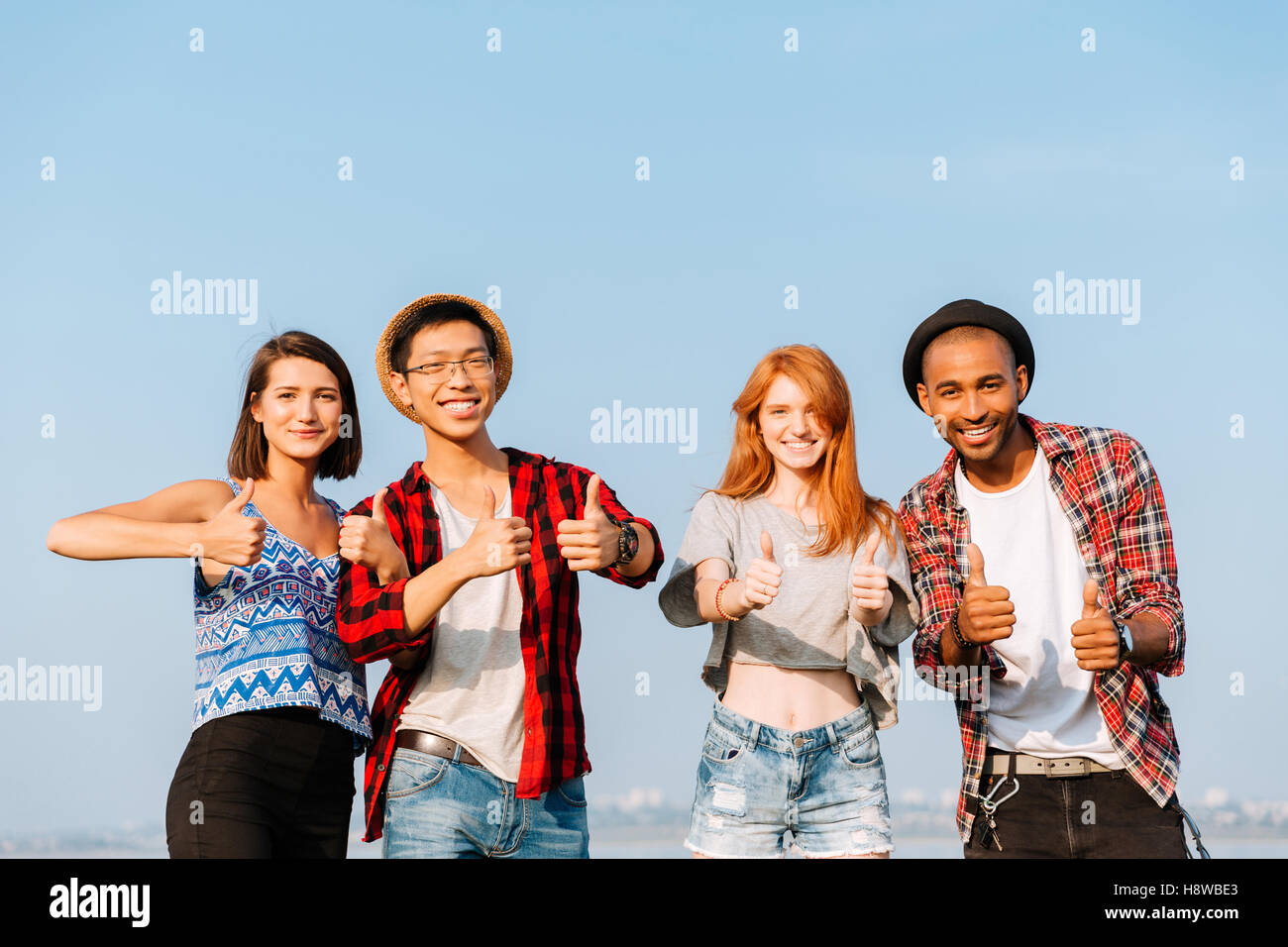 Multiethnic group of smiling young friends standing and showing thumbs ...