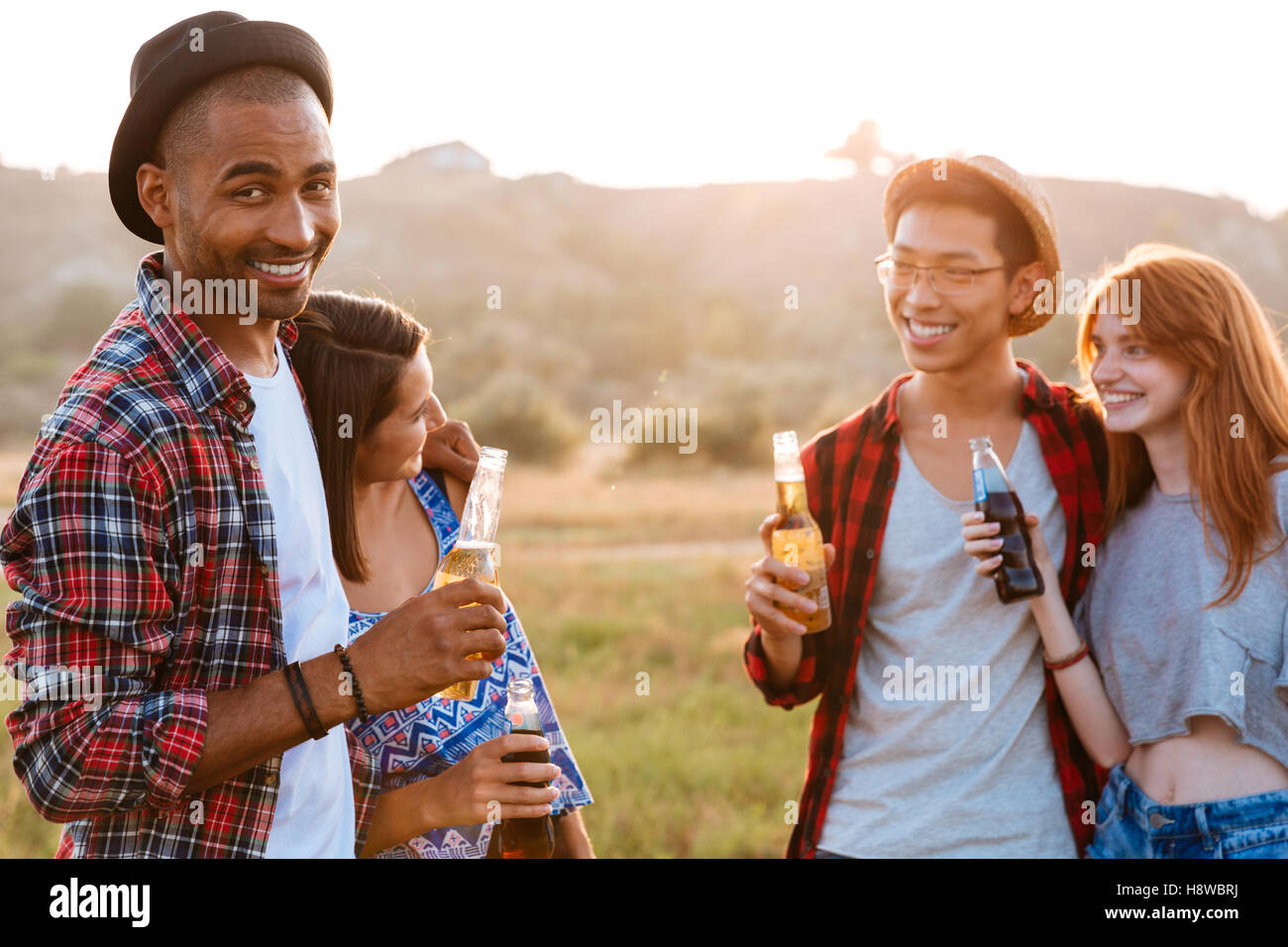 Two cheerful multiethnic couples drinking beer and soda outdoors Stock Photo
