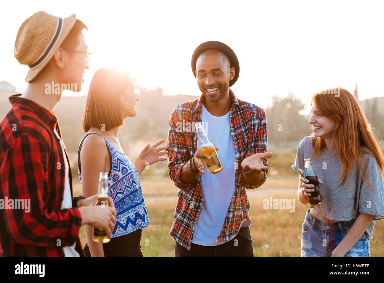 Multiethnic group of cheerful young people with beer and soda talking and laughing outdoors Stock Photo