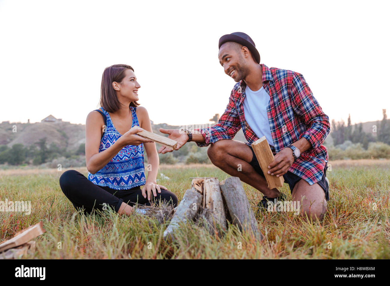 Cheerful young couple smiling and making campfire outdoors Stock Photo